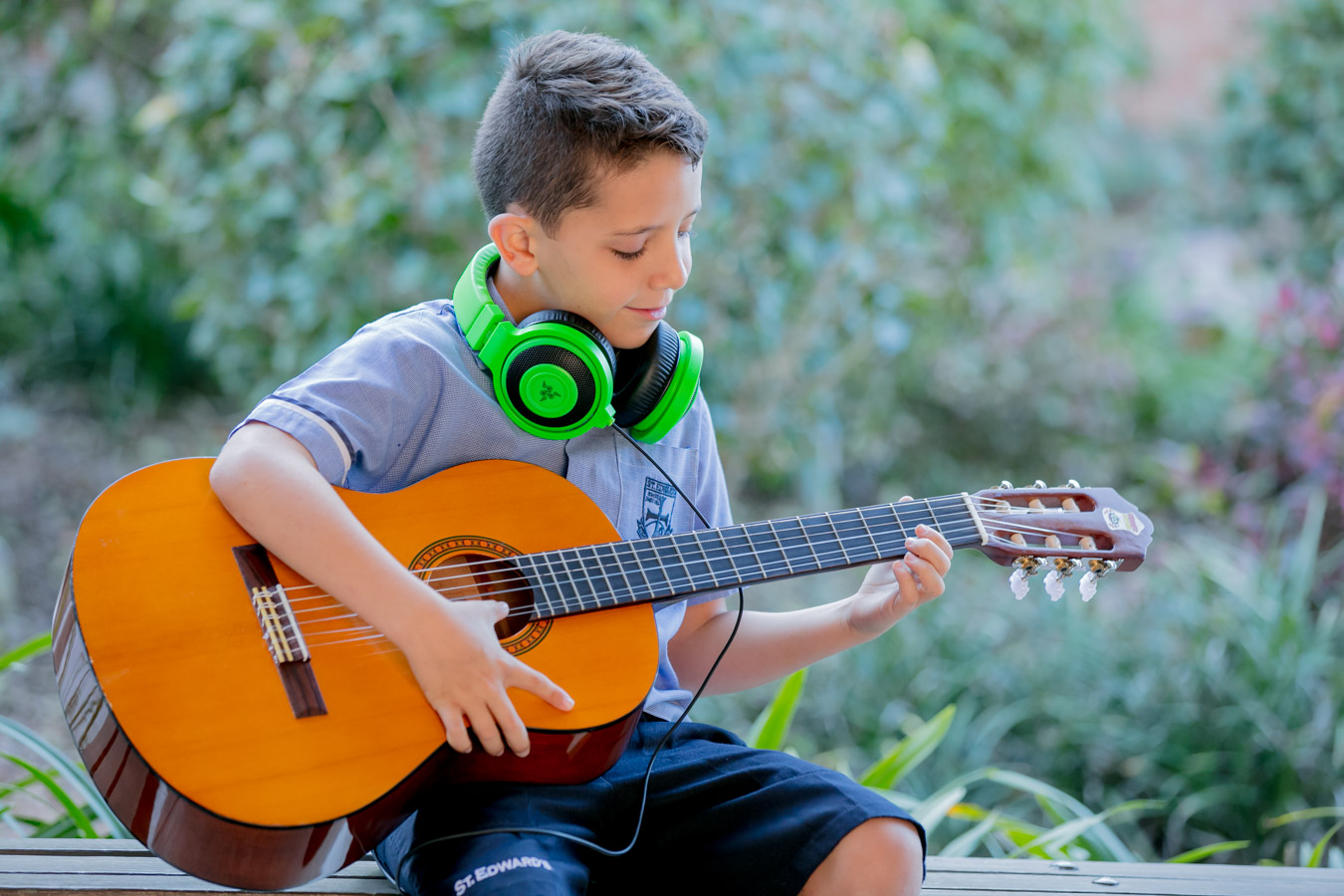 Student playing guitar outdoors wearing headphones promoting creativity music learning and individual skill development
