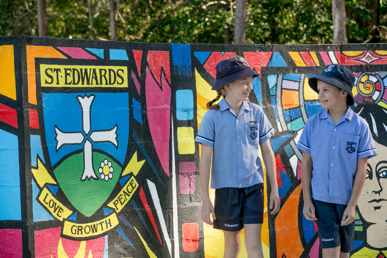Students in school uniform walking together in front of a colourful mural featuring the St Edward’s crest highlighting friendship belonging and school identity