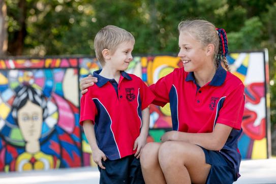 Older student kneeling beside a younger student in school uniform showing care mentoring and inclusive relationships within the school community