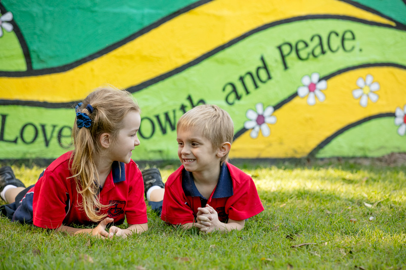 Students lying on grass together in front of a mural highlighting love growth and peace and reflecting friendship and a strong sense of belonging