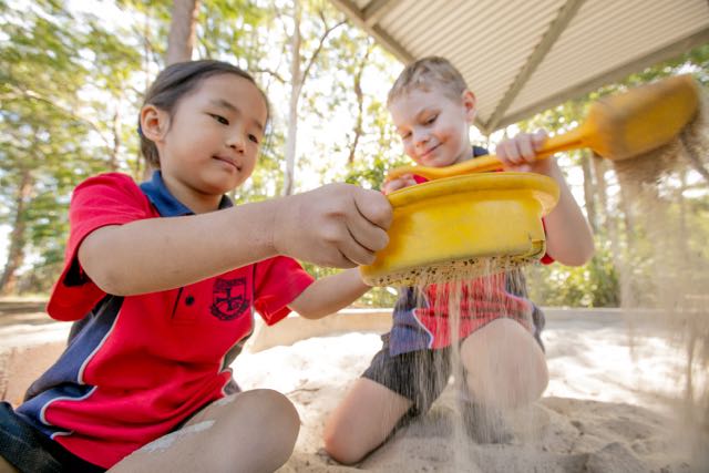 Students playing in a sandpit outdoors promoting sensory play exploration and active learning