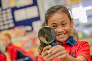Student using a magnifying glass in a classroom supporting curiosity investigation and inquiry based learning