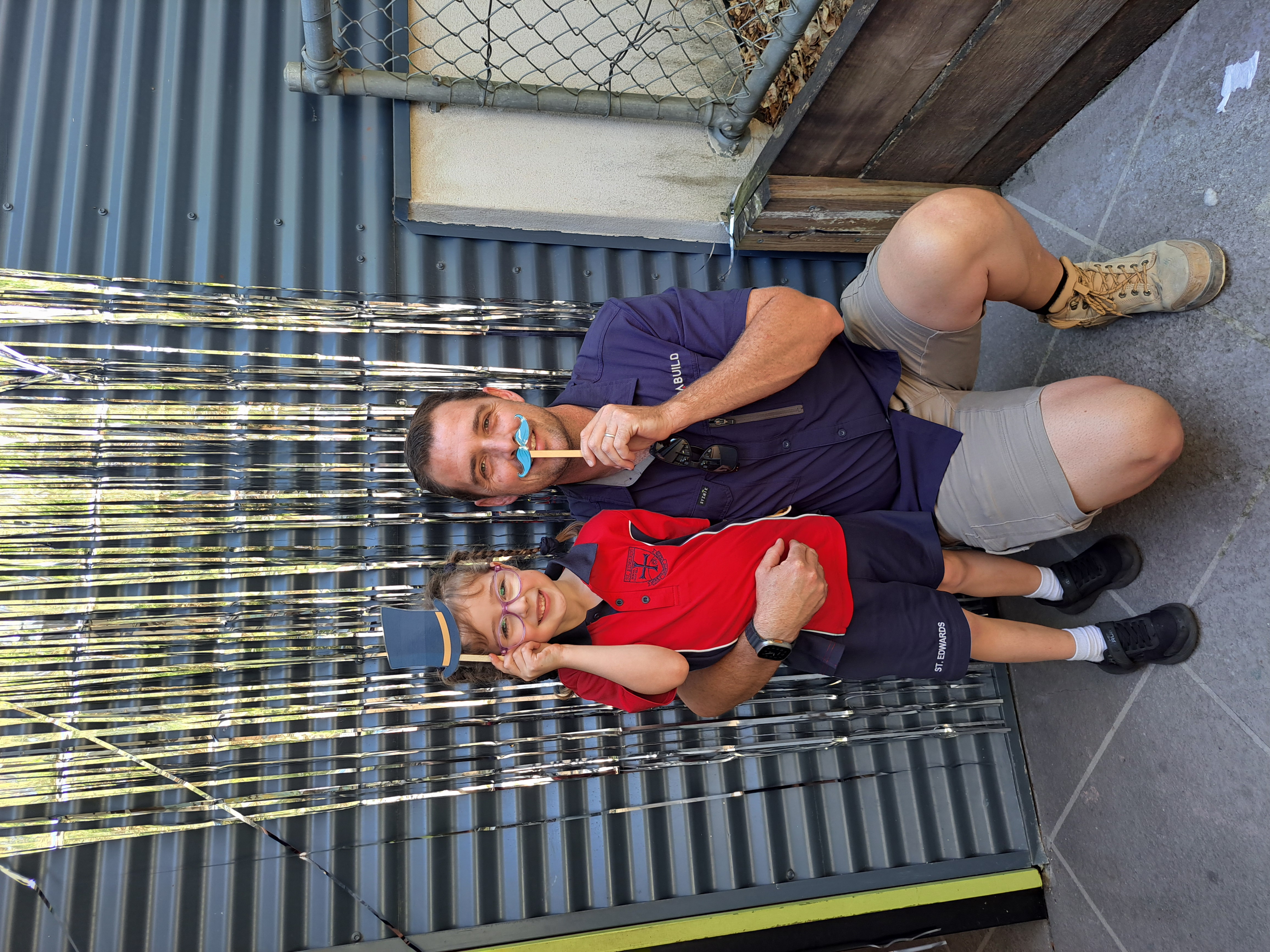 Father and child posing together during a school Father’s Day activity using playful props highlighting family connection community engagement and a welcoming school environment