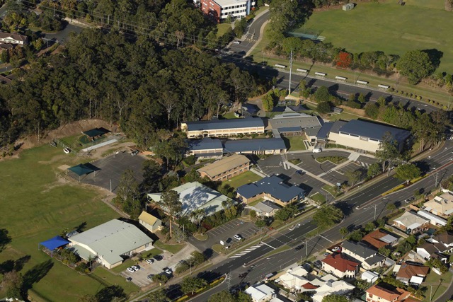 Aerial view of a school campus showing classroom buildings sporting facilities and surrounding residential area highlighting the scale and layout of the learning environment