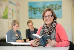 Staff member holding a book in a classroom setting highlighting supportive teaching and engagement in student learning